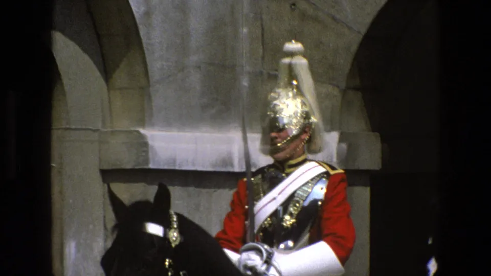 Mounted ceremonial guard in red uniform and polished helmet sits on a black horse beside a shadowed stone archway.