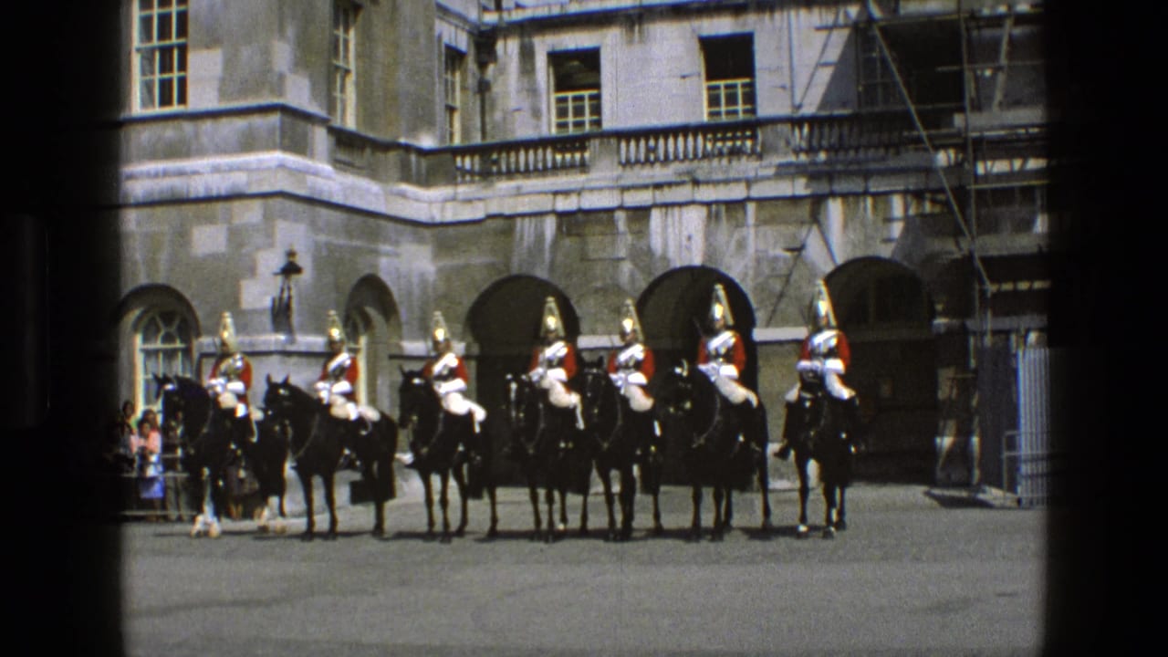 Mounted guards in red tunics line up outside a large stone building with arches.
