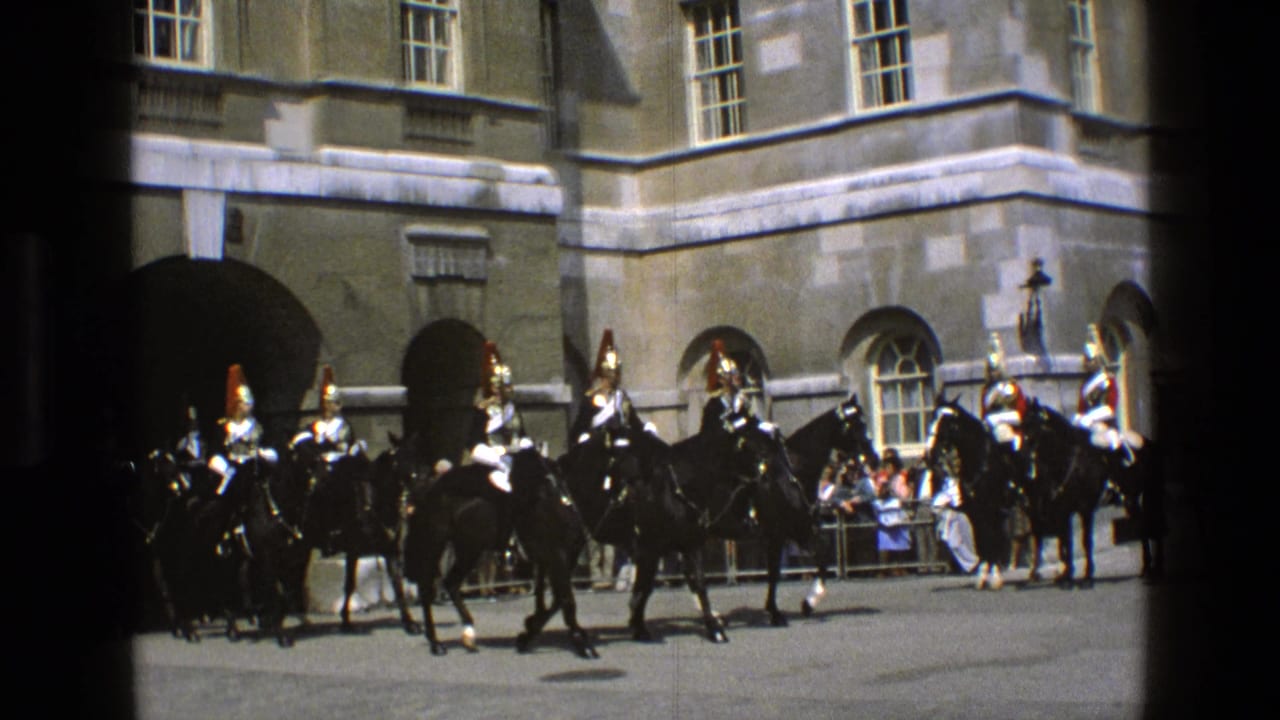 1969 England frame with ceremonial riders on black horses moving across a courtyard before arched stone entrances and onlookers.