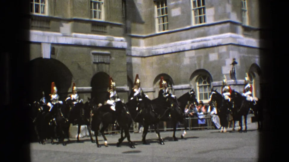 1969 England frame with ceremonial riders on black horses moving across a courtyard before arched stone entrances and onlookers.