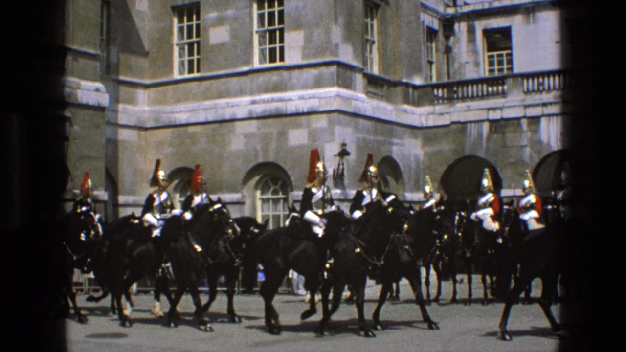 Mounted ceremonial guards on dark horses ride in formation past a palace-like stone facade in 1969 England footage.