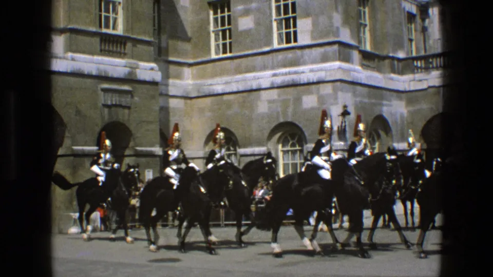 In England in 1969, armored ceremonial riders on dark horses pass through a stone courtyard as spectators watch behind barriers.
