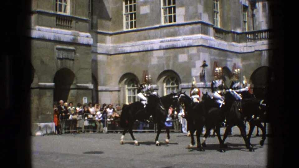 Armored riders on black horses move through the courtyard while a small crowd watches from behind barriers in England, 1969.
