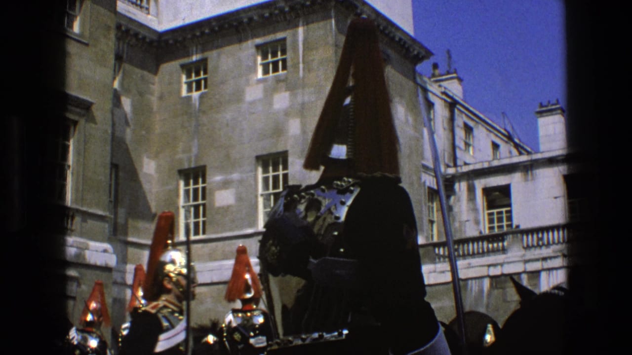 Mounted guards in plumed helmets stand before a stone building in bright sunlight.