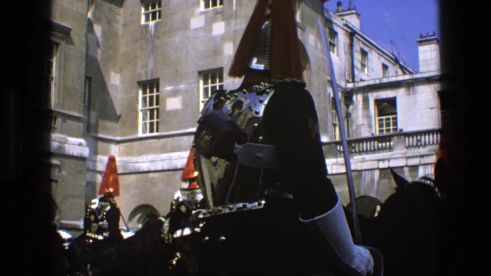 A close 1969 England home-movie view frames a mounted ceremonial guard's armor and plume with other riders behind.