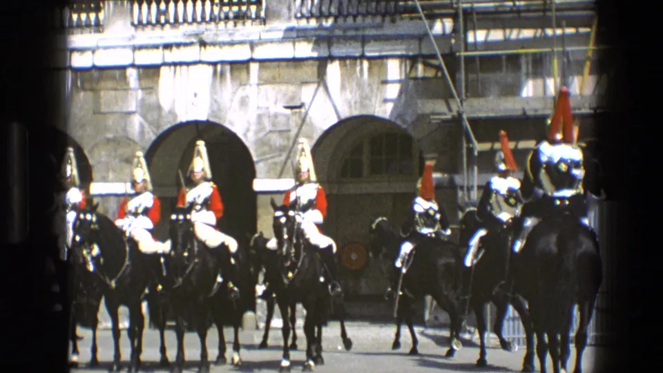 1969 England 8mm frame showing ceremonial mounted soldiers in red tunics and plumed helmets before arched stone doorways.