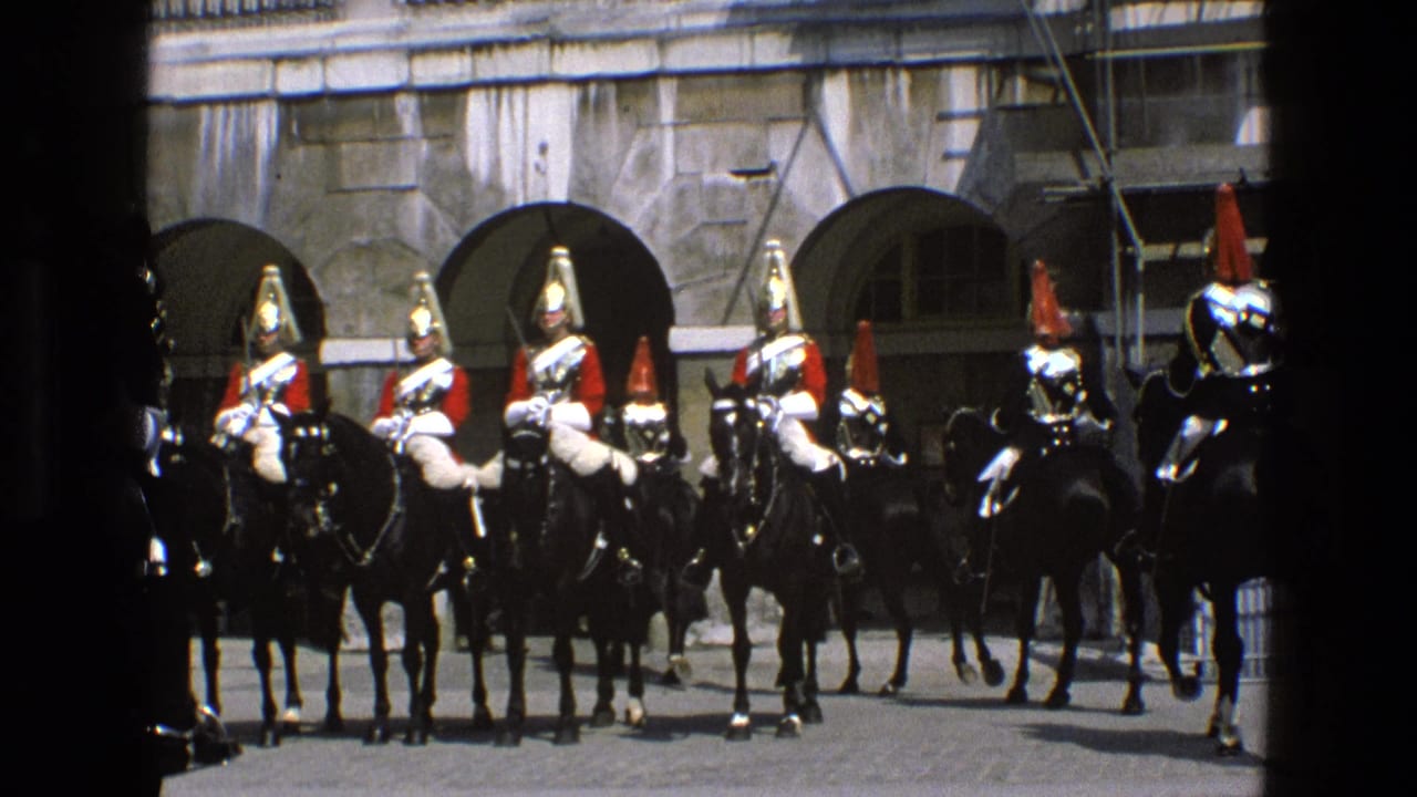Ceremonial mounted guards in red and white uniforms remain aligned on black horses in an English stone courtyard.