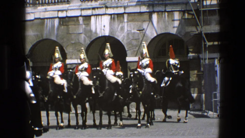 Ceremonial mounted soldiers on black horses face forward in an English courtyard, with scaffolding visible near the stone facade.