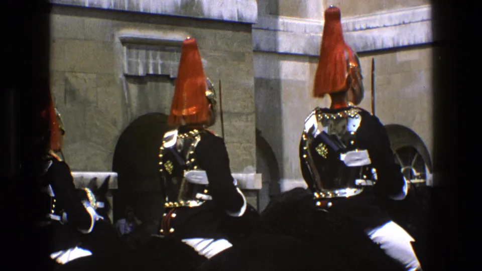 1969 England 8mm frame showing mounted ceremonial guards with red plumes, polished breastplates, and black horses near stone architecture.