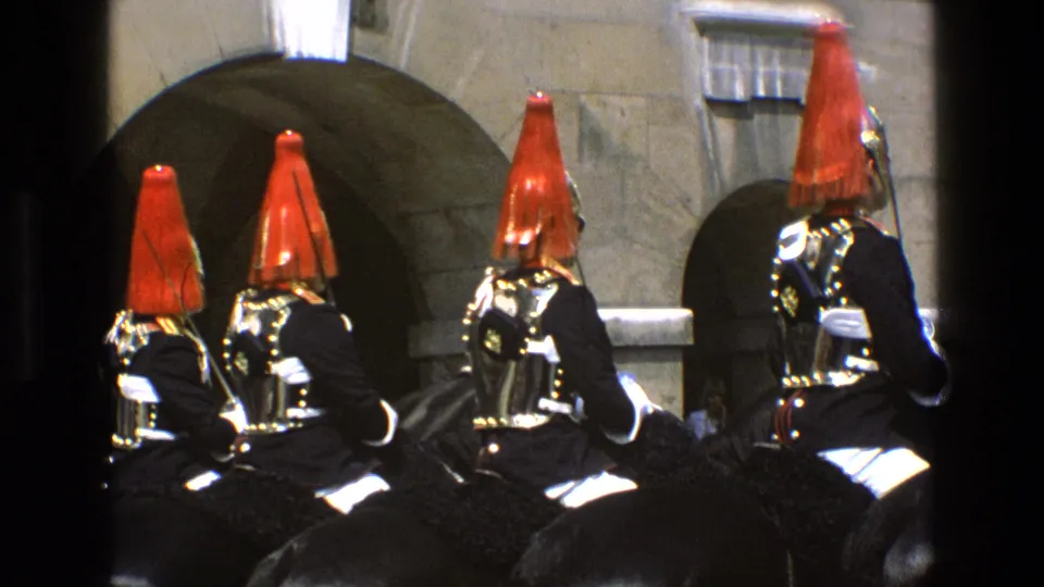 A row of mounted ceremonial soldiers in 1969 England appears before stone arches, with red plumes and armor catching the light.