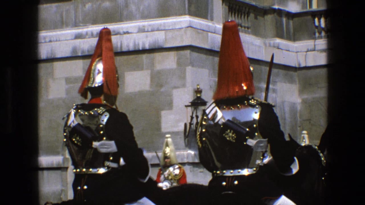 Mounted guards in ceremonial uniforms face a stone building.