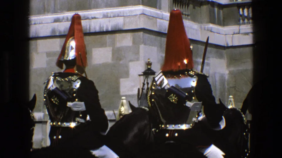 1969 England frame showing mounted ceremonial guards holding position, with red plumes, dark uniforms, bright metal armor and horses visible.
