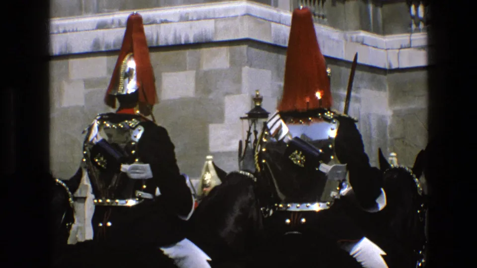 1969 England footage showing mounted ceremonial soldiers in red plumes, polished armor, and dark uniforms near stone architecture.