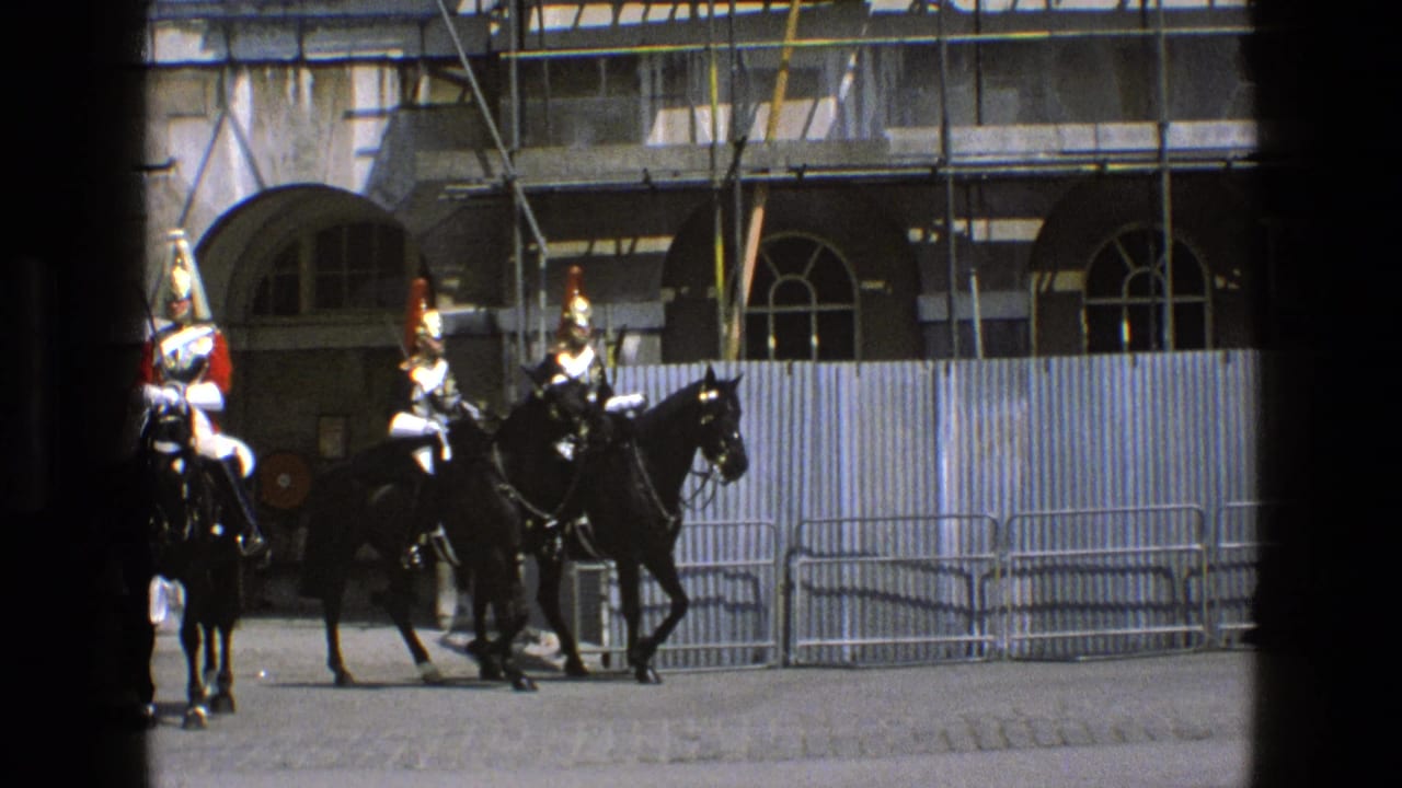 Mounted guards ride past scaffolding and metal barriers outside a stone building.
