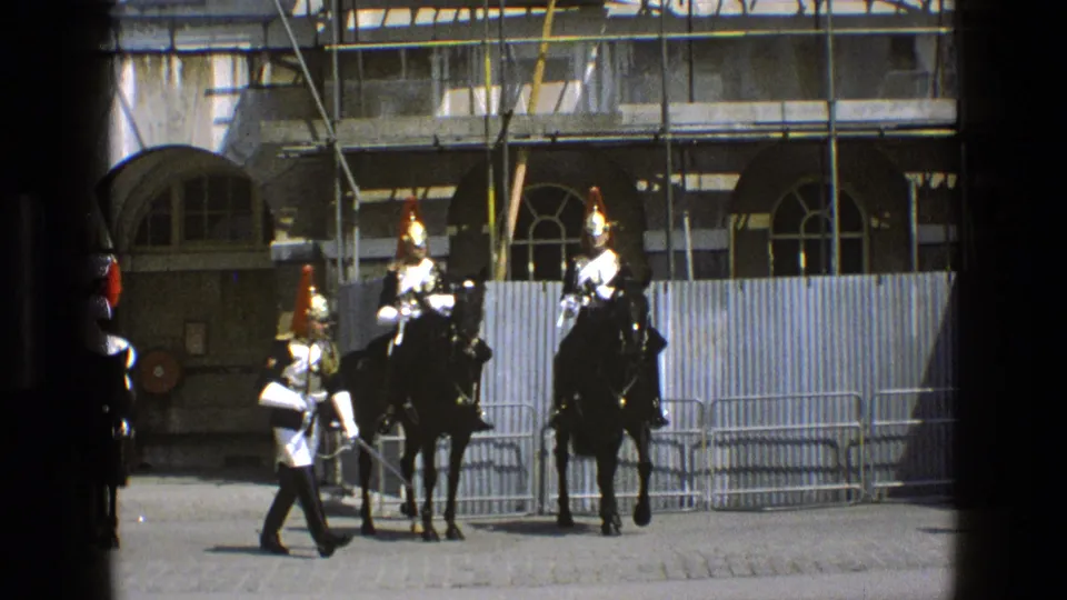 A ceremonial guard on foot crosses before mounted soldiers on black horses during a formal procession in 1969 England footage.