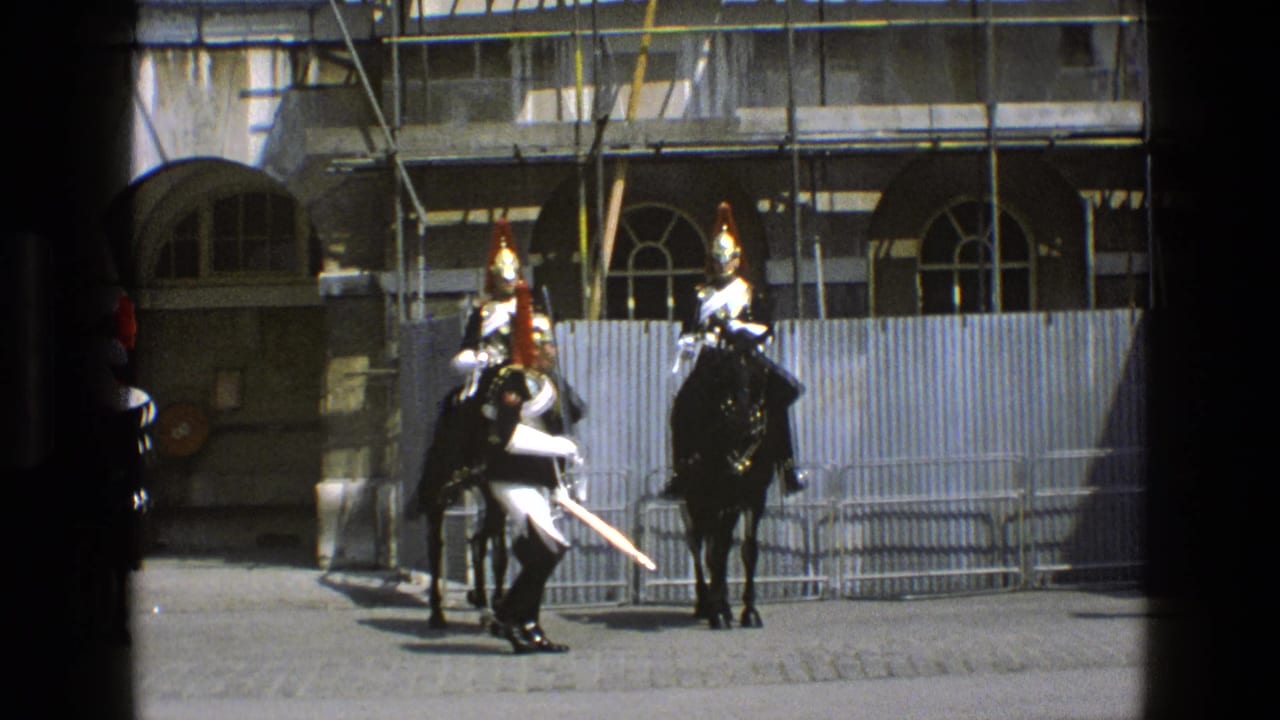 Two mounted ceremonial guards and a soldier with a sword in front of barriers and scaffolding.