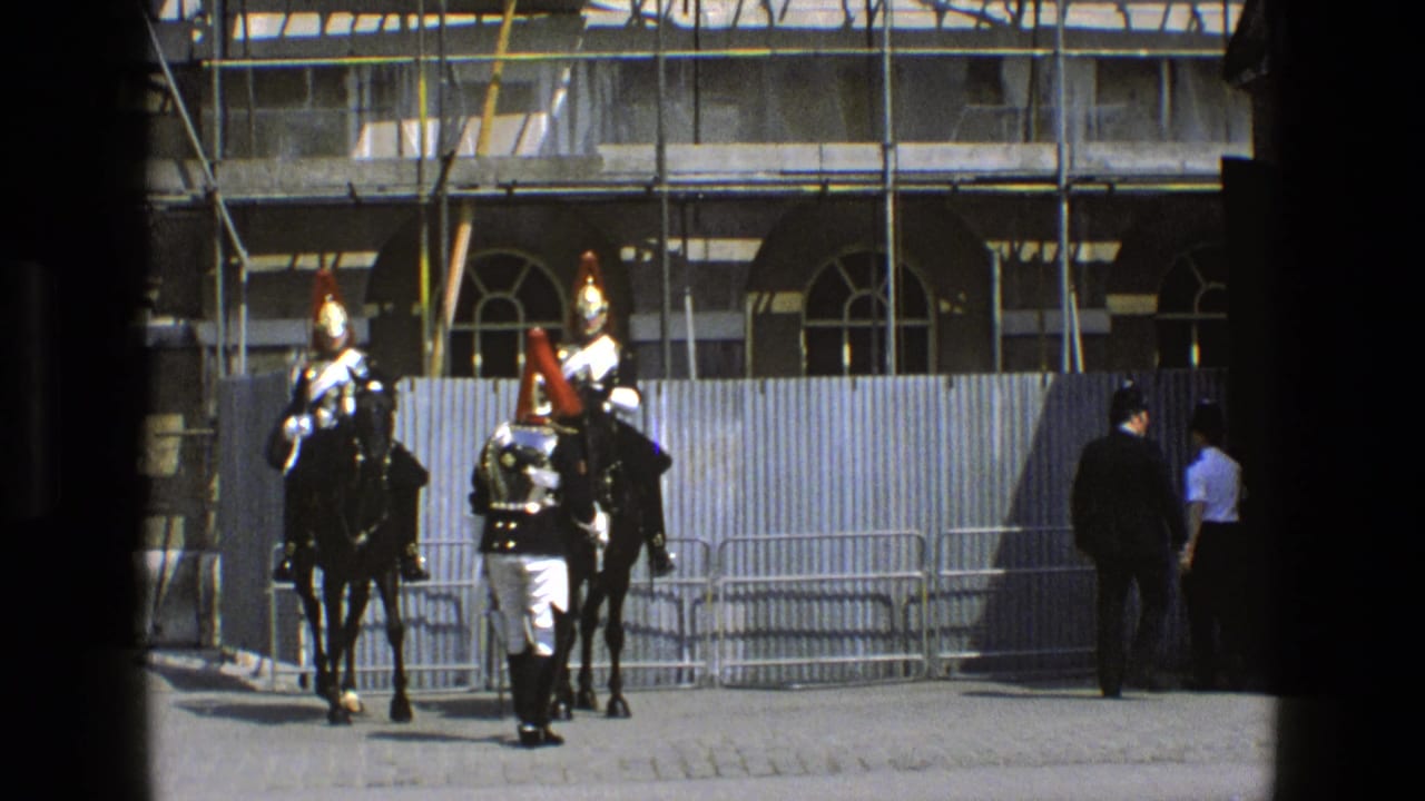 A soldier faces two mounted guards beside metal barriers and a scaffolded building.