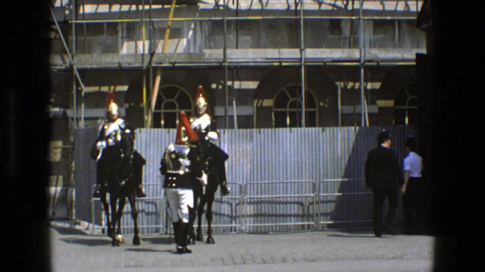 1969 England frame with a soldier in dress uniform facing two mounted ceremonial guards in front of barriers and scaffolding.