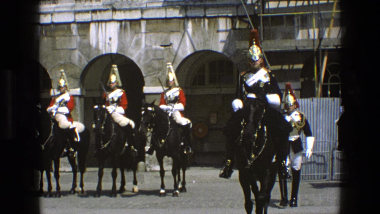 Mounted ceremonial guards in polished helmets and breastplates sit on black horses before arched stone doorways in England, 1969.