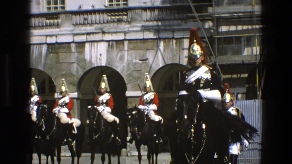 1969 England home-movie frame of ceremonial guards on black horses, with one mounted figure passing closer in the foreground.