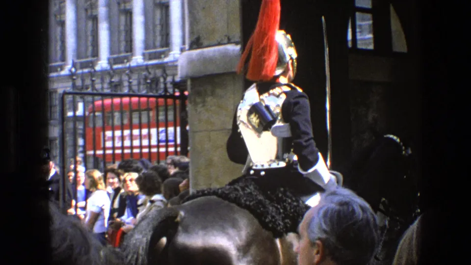 Rear view of a ceremonial mounted guard with a red plume near spectators gathered by a fence in England, 1969.