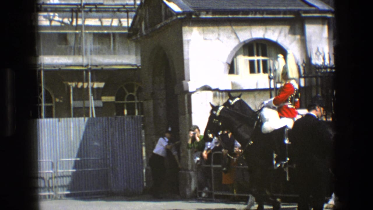Mounted guard in red coat rides a black horse near a stone courtyard building.