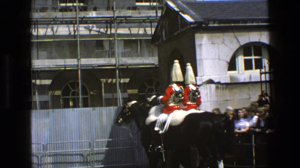 1969 England 8mm frame showing two mounted ceremonial guards in red coats and tall hats before spectators and scaffolding.
