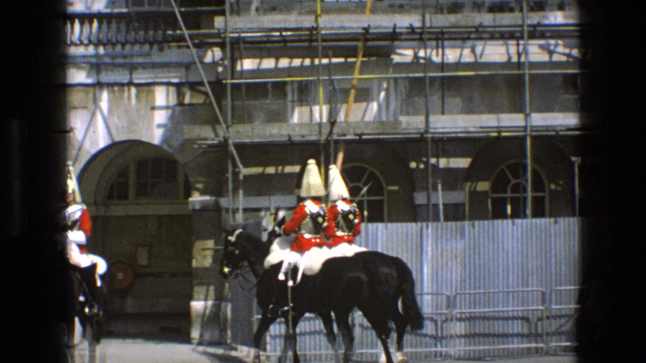Ceremonial riders in red coats and tall gold-topped helmets pass arched stone doorways in England, filmed on 8mm in 1969.