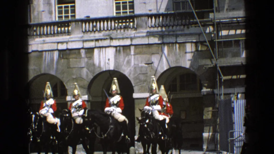 Mounted ceremonial guards on black horses form a small group before a stone building, with scaffolding visible in 1969 England 8mm footage.