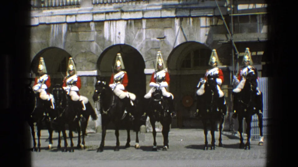 In England in 1969, a line of ceremonial cavalry faces the camera on black horses, framed by stone arches and construction scaffolding.