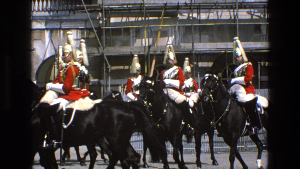 Mounted ceremonial guards in red coats ride black horses past a stone building.