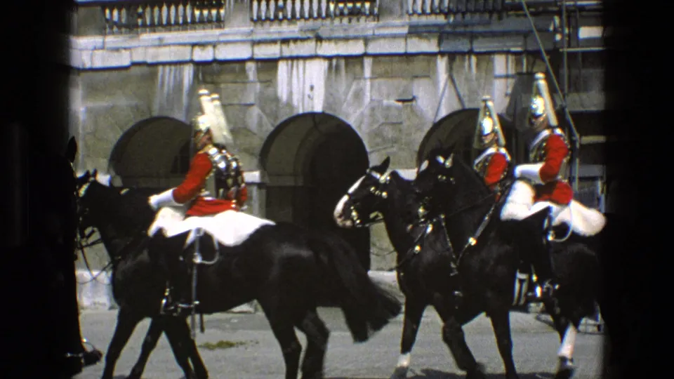 Ceremonial guards on black horses move across the frame before stone arches, captured from a visitor's 1969 England viewpoint.