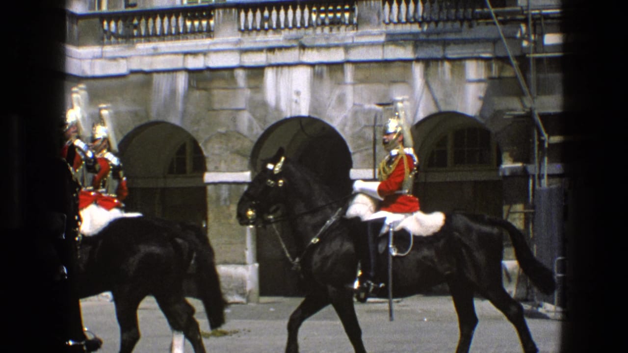 In 1969 England footage, a red-uniformed mounted guard on a black horse moves past a grand stone wall with arched openings.
