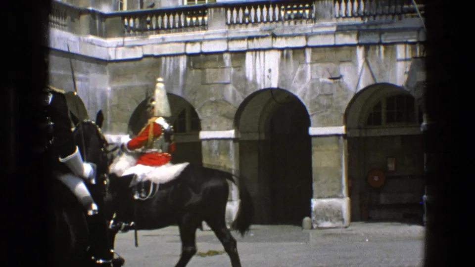 In 1969 England footage, a mounted guard in red uniform passes arched stone doorways while dark foreground edges frame the home-movie view.