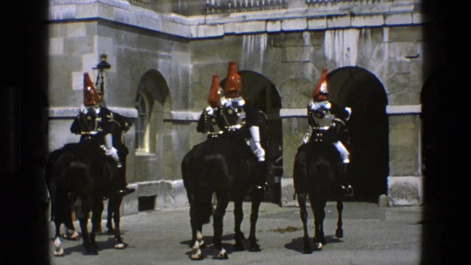 1969 England frame showing three mounted guards in ornate helmets and armor riding through an arched stone courtyard.