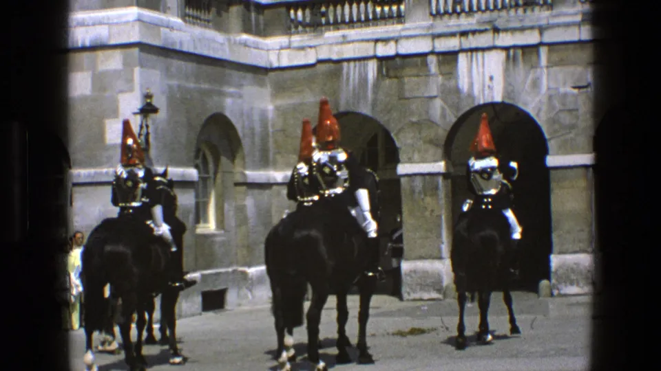Late-frame 1969 England view of mounted ceremonial guards on black horses passing stone arches as bystanders watch nearby.
