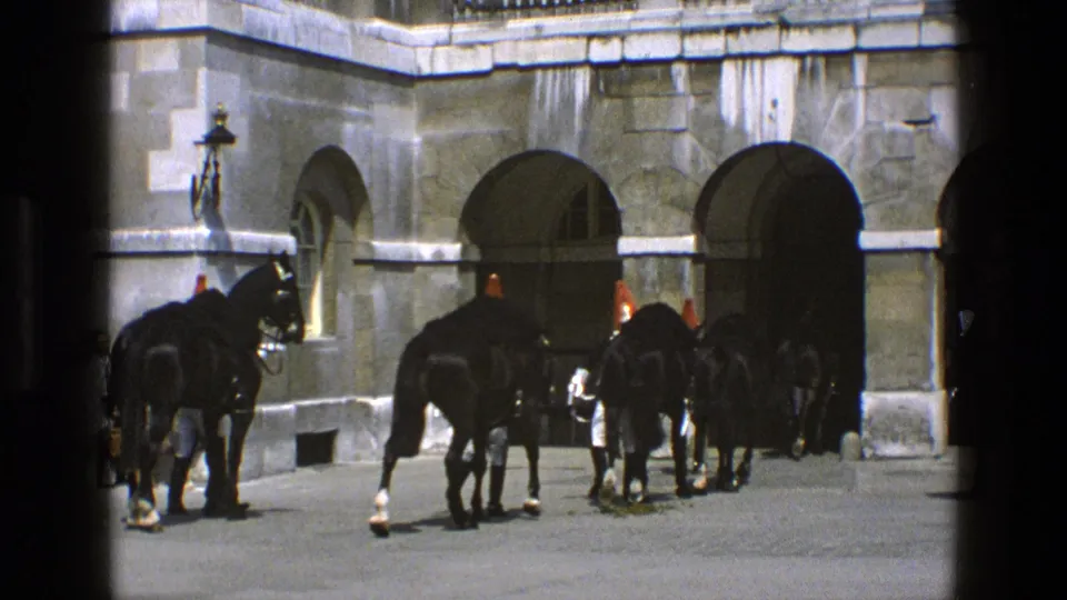Ceremonial horses and guards cluster near a broad stone arch in this 1969 England 8mm home-movie frame.