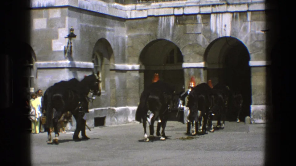 In 1969 England footage, ceremonial mounted guards and black horses gather by arched stone entrances while visitors watch nearby.