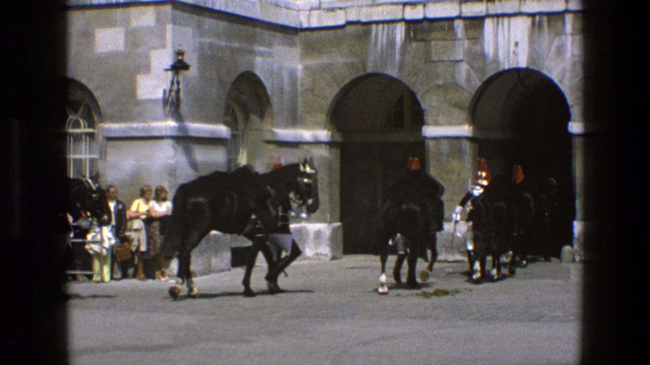 A black horse is led across a courtyard while other horses and guards wait near stone archways.