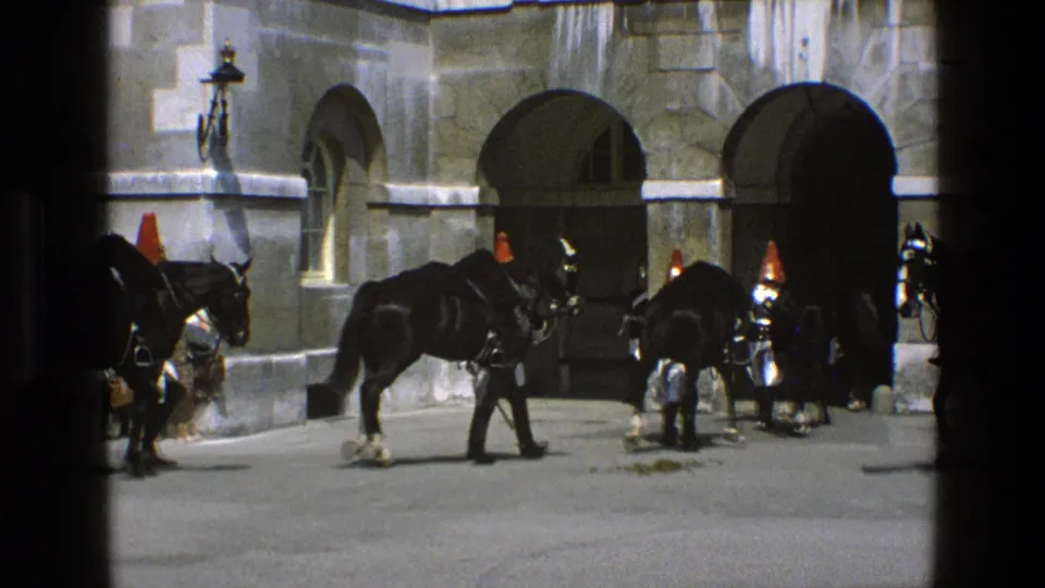 Ceremonial mounted guards and black horses cluster near arched stone openings in this supplied 1969 England home-movie frame.