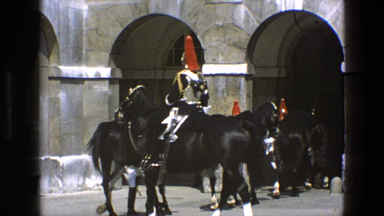 Ceremonial riders on black horses move beside arched stone openings.