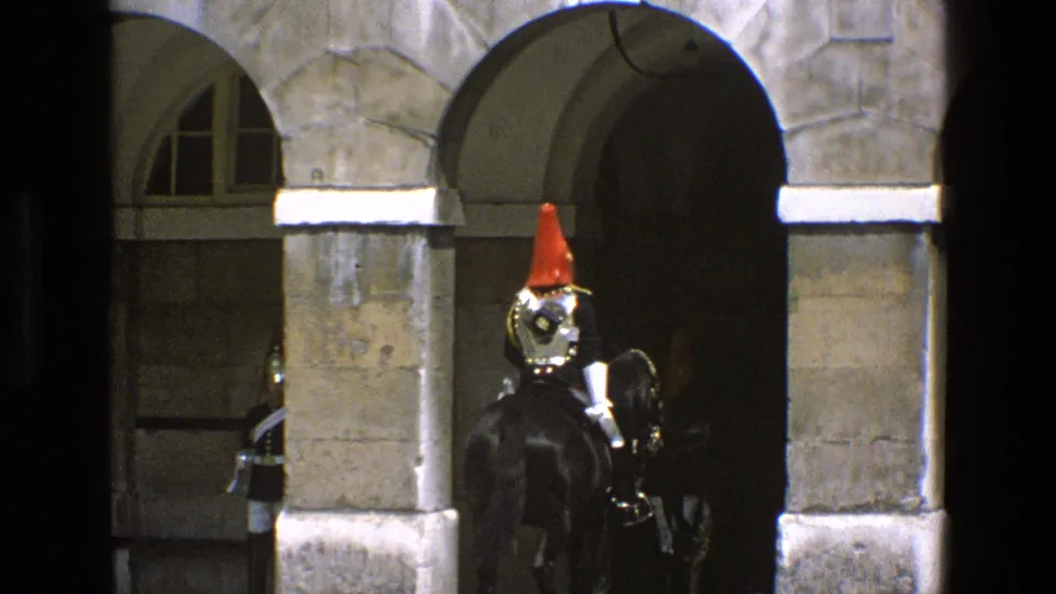 A mounted guard in polished armor and a red plume rides away toward a dark stone arch, with another horse partly visible at the side.