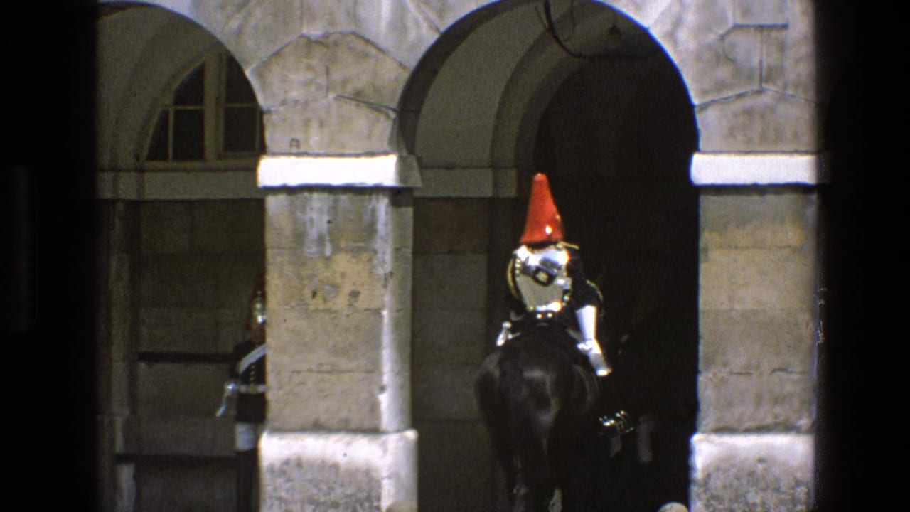 In England 1969 footage, a mounted guard with a red plume rides a dark horse into a shadowed stone archway.