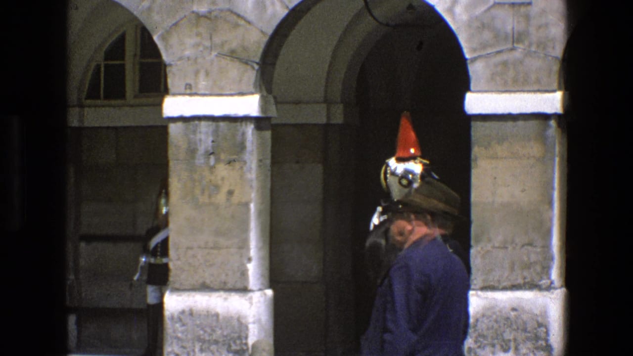 A civilian in a hat stands near the arch as the red-plumed mounted guard is partly visible in England 1969 footage.