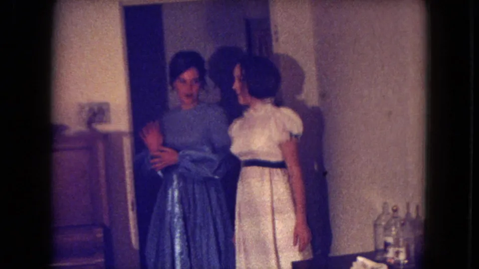 Inside a private room, the woman in the blue gown appears to wave or gesture as the woman in white stands nearby in the 1969 Fort Wayne footage.