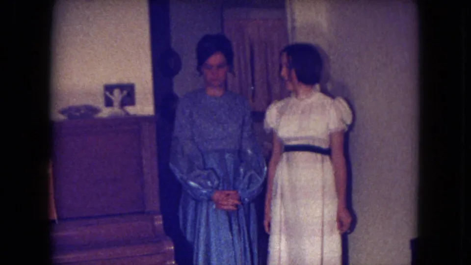 The two women stand close together in a Fort Wayne interior, with a piano and curtains behind them in the 1969 8mm footage.