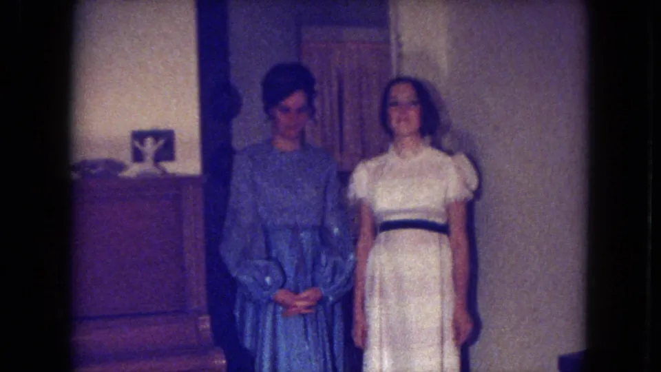 Two young women pose in formal dresses inside a private Fort Wayne room, with late-1960s hair and dress details visible.
