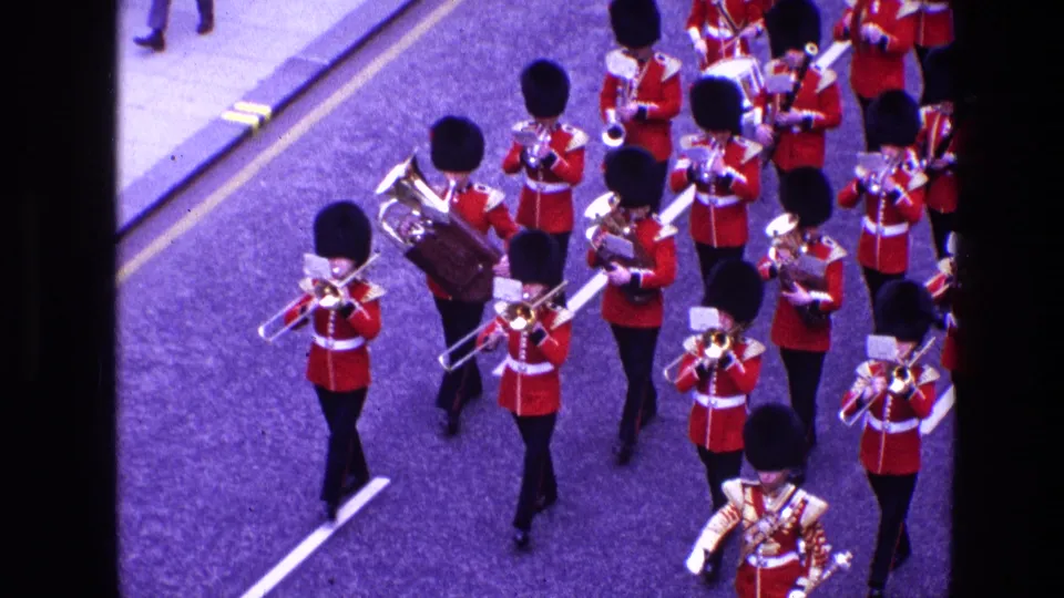 Closer 8mm frame of the 1969 Ireland parade, with red-coated musicians marching in rows and playing brass instruments.