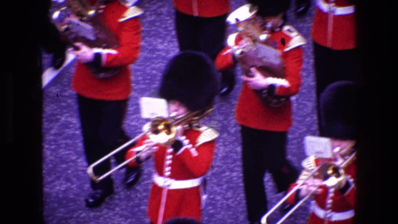 Marching band members in red tunics play trombones while moving in formation.