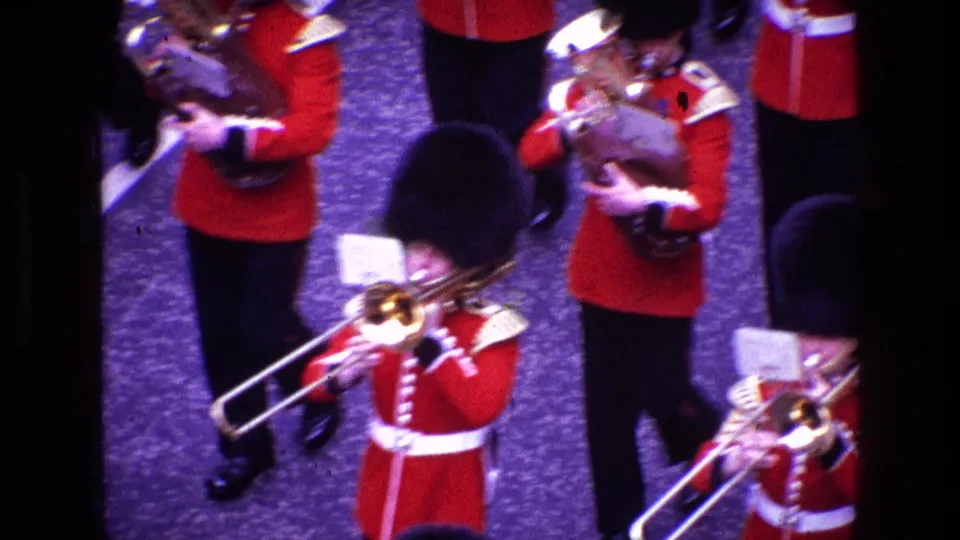 Ceremonial band members in red uniforms and tall black hats play trombones during the 1969 home-movie parade footage.